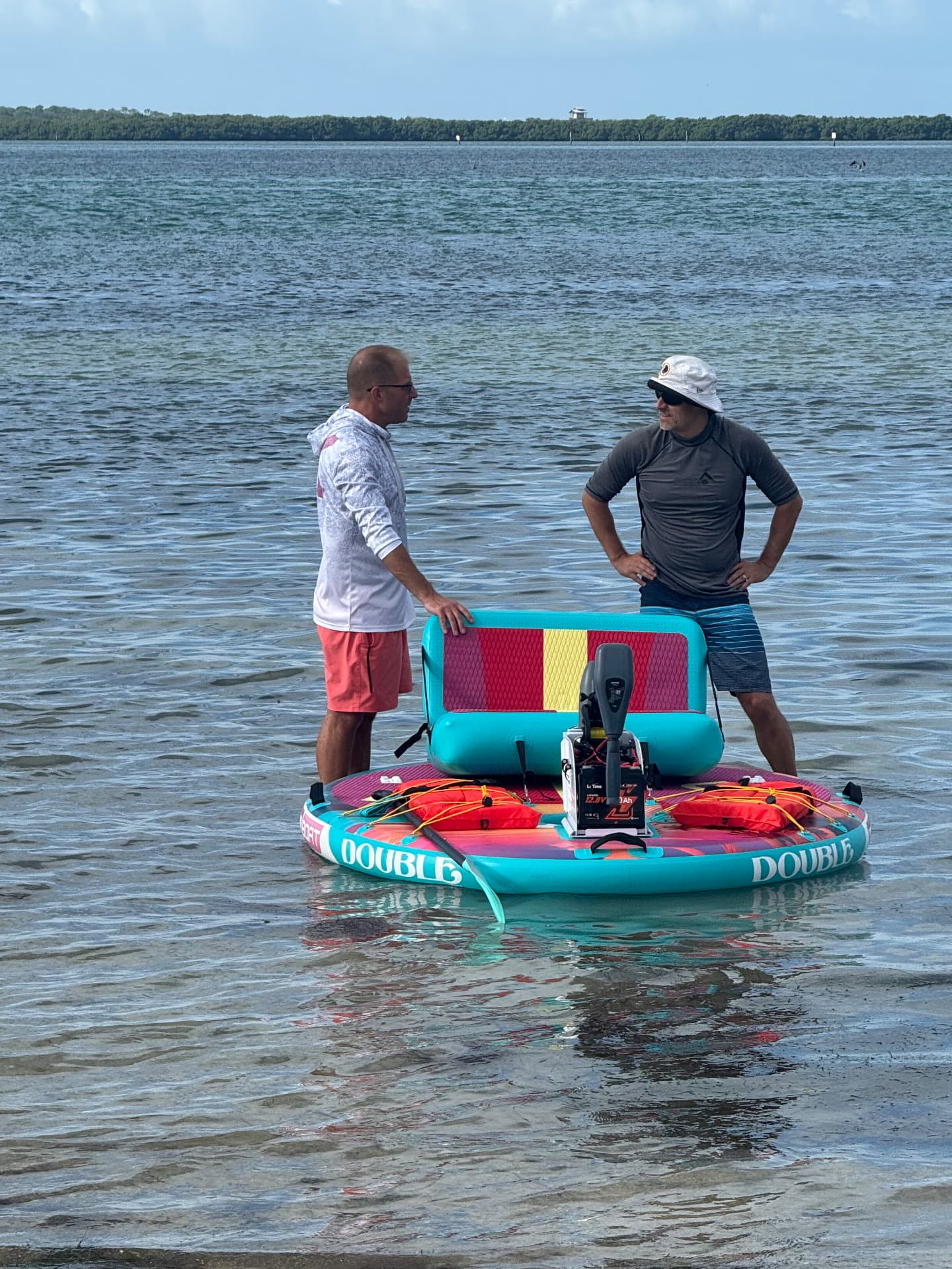 Two men standing with a colorful Double GoBoat in shallow water, with the entire boat and DOUBLE lettering visible