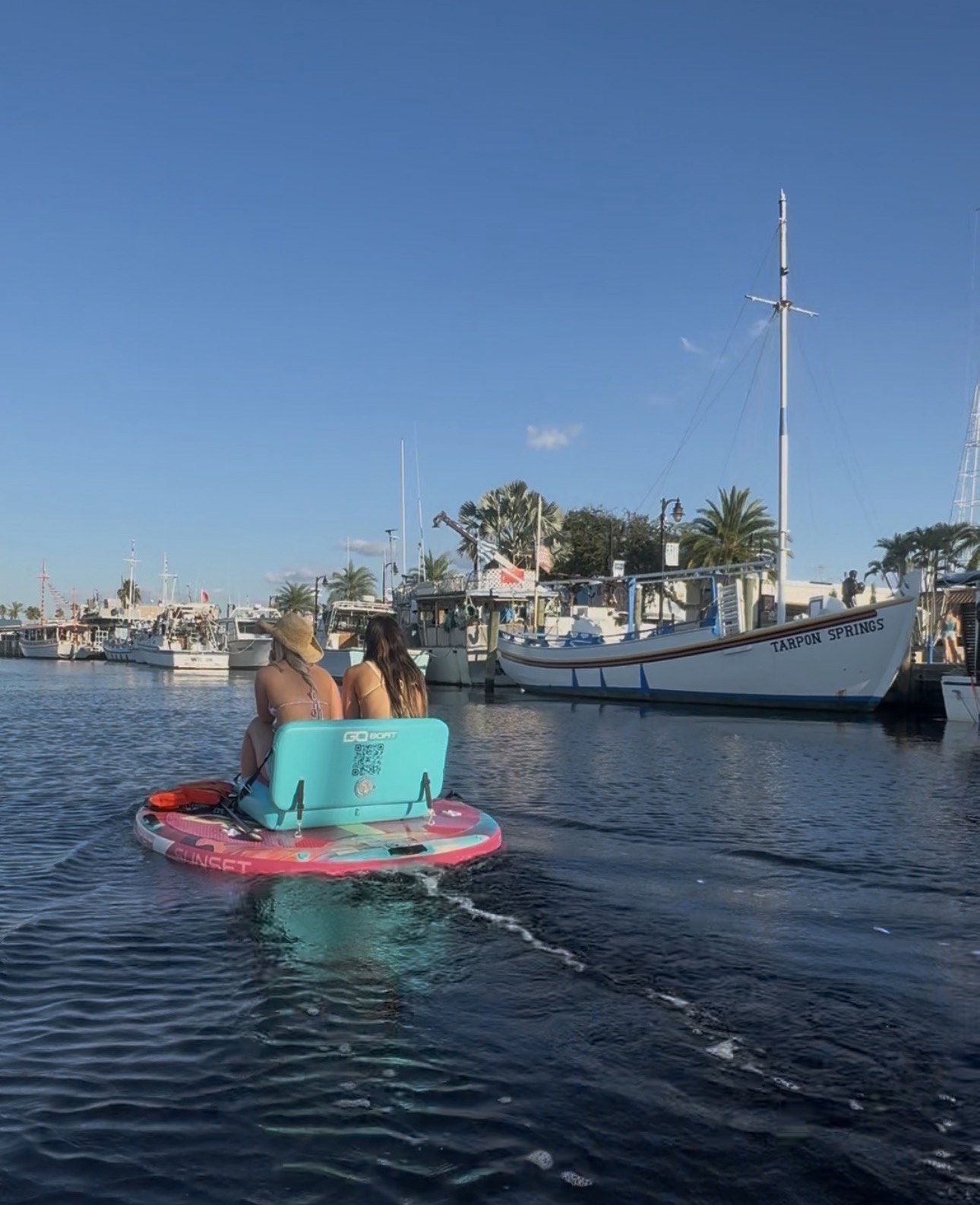 Two friends cruising a round electric GoBoat past the historic Tarpon Springs sponge boats